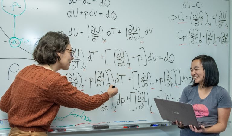 Professor showing differential equation problem to student at whiteboard.